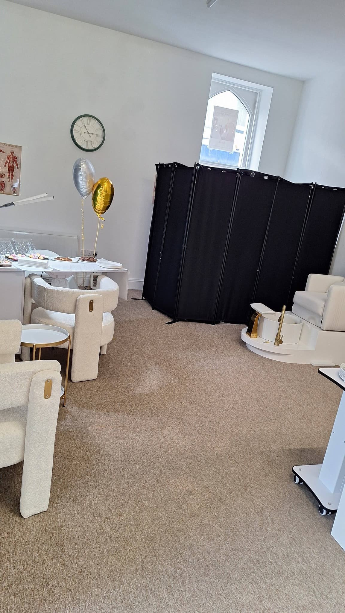 Lounge area with bouclé chairs, gold-accent pedicure station and a black privacy screen.