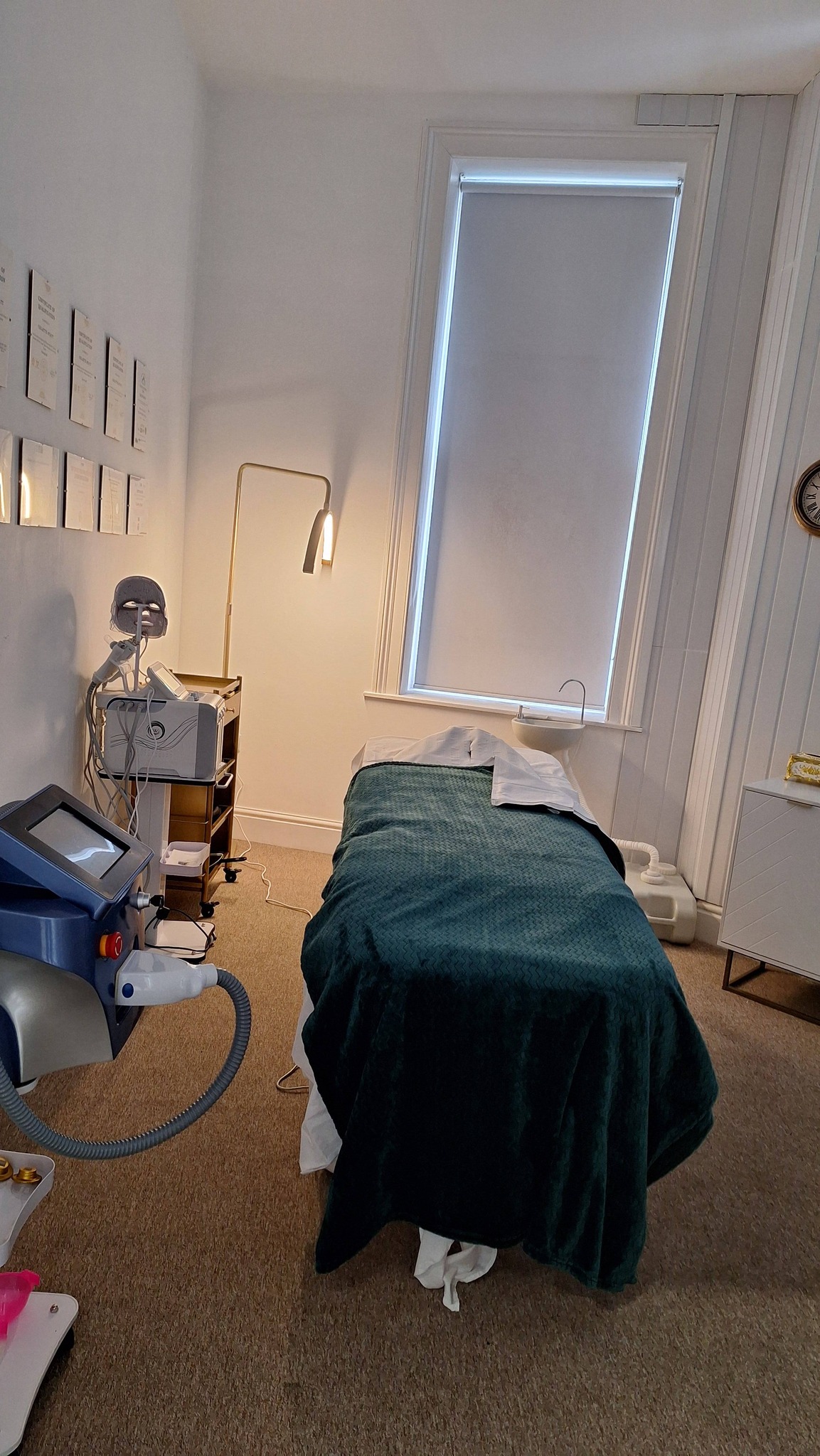 The Beauty Bank Clinic treatment room — gold arc lamp, white panelled walls, branded pillow on the treatment bed.
